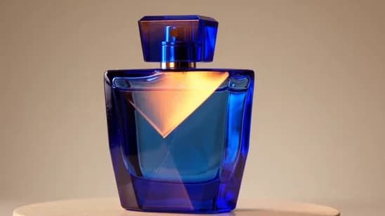 A complete blue glass perfume bottle on a warm studio pedestal.